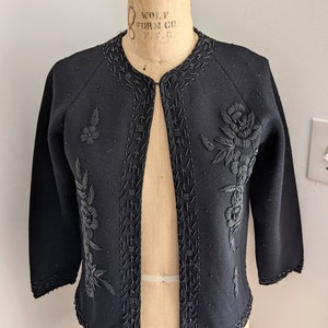 May include: A black cardigan with a beaded floral design. The cardigan is open in the front and has long sleeves.