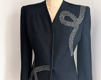 May include: A black blazer with a silver rhinestone design. The design is a curved line that resembles a snake or ribbon.