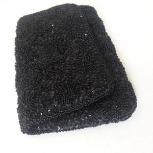 May include: A black beaded clutch purse with a fold-over closure. The purse is covered in small black beads and sequins.