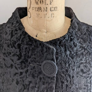 Könnte beinhalten: Nahaufnahme einer schwarzen Pelzjacke mit einem einzigen Knopfverschluss. Das Fell ist in einem lockigen, strukturierten Stil.