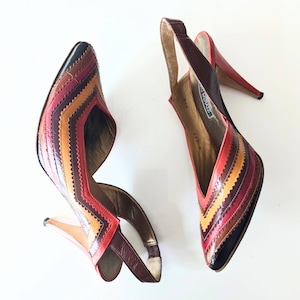 May include: A pair of red, brown and yellow striped heeled shoes with a slingback strap. The shoes have a pointed toe and a high heel.