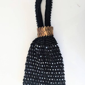 以下が含まれることがあります： 金色のチェーンのハンドルが付いた小さな黒いビーズの財布。財布は、繊細で複雑なデザインを作り出すために、一緒に織られた小さな黒いビーズで作られています。