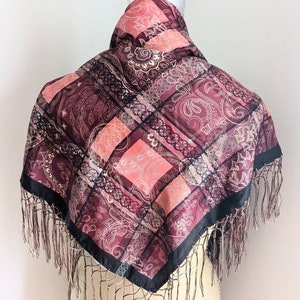 May include: A burgundy and pink paisley patterned silk scarf with black trim and fringe.