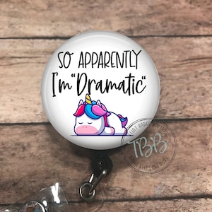 May include: White badge reel with a white button featuring a cartoon unicorn and the text "So Apparently I'm "Dramatic"".