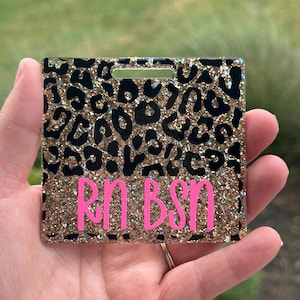 May include: A gold glitter and black leopard print badge holder with a pink glitter "RN BSN" inscription.