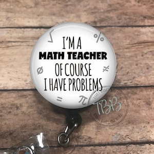May include: White round badge reel with a black retractable cord and a clear crystal charm. The badge holder features a white background with black text that reads "I'm a Math Teacher Of Course I Have Problems" and various math symbols. The badge reel also has a black and white logo that reads "That Badge Boutique TBB Badge Reels and More."