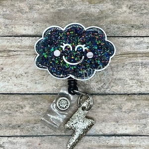 May include: A black glitter cloud with a white outline and a smiling face, attached to a silver glitter lightning bolt charm and a retractable badge reel.