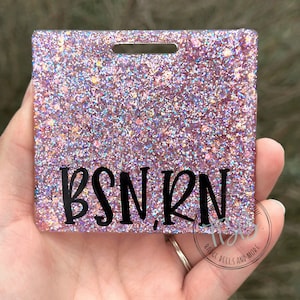 May include: A pink glitter badge holder with a hole for a lanyard. The text "BSN, RN" is printed in black on the front of the badge holder.