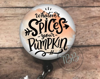 Può includere: Un rotolo per badge rotondo bianco con uno sfondo ad acquerello in tonalità arancio e pesca. Il testo "Whatever Spices Your Pumpkin" è scritto in corsivo nero. Il rotolo per badge è attaccato a un porta badge in plastica trasparente con un cristallo di strass.