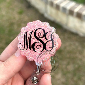May include: Pink glitter badge reel with a black monogram "M.S.S." and the text "Tila's Badge Boutique" and "Badge Reels and More".