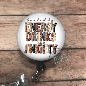 May include: A white round badge reel with a black retractable cord and a clear plastic badge holder. The badge reel features a leopard print design with the text "fueled by energy drinks and anxiety".