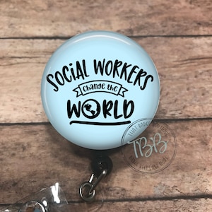 May include: A light blue badge reel with a white background and black text that reads "Social Workers Change the World" with a small globe graphic. The badge reel has a clear plastic badge holder and a black retractable cord.