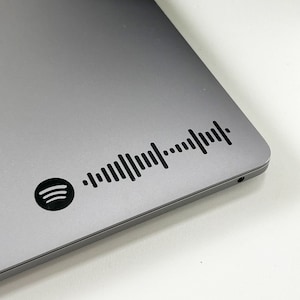 May include: A silver laptop with a black Spotify logo and a black barcode sticker.