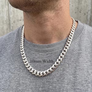 May include: A silver-coloured cuban link chain necklace with a polished finish. The chain features interlocking oval links and is clearly labelled with the text 10mm Width, indicating the specific measurement of the chain links as shown in the image.