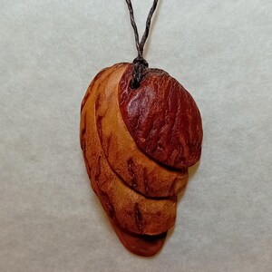 Pięknie wykonany wisiorek ze sztucznej skamieliny, ręcznie wyrzeźbiony z pestki awokado, przy użyciu technik upcyklingu.