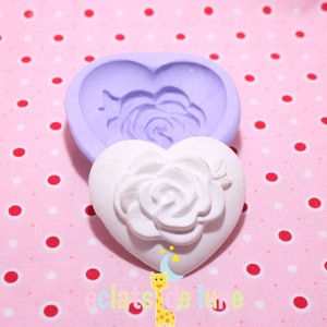 Puede incluir: Un molde de silicona morado en forma de corazón con un diseño de rosa en relieve, y un molde en forma de corazón blanco con el mismo diseño.