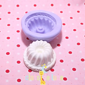 Puede incluir: Un molde de silicona morado para hornear un pastel bundt. El molde se muestra junto a un pastel blanco hecho en el molde.