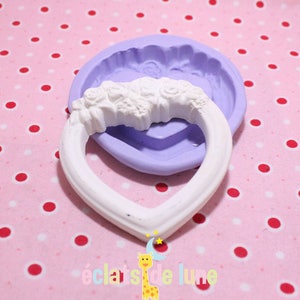 Puede incluir: Un marco blanco en forma de corazón con un diseño floral en la parte superior. El marco está sobre un fondo de lunares rosa y blanco. El marco está hecho de silicona y se utiliza para hacer manualidades.