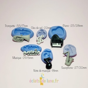 Puede incluir: Molde de silicona con seis diseños diferentes de instrumentos musicales: una trompeta, una clave de sol, un piano, una nota musical, un saxofón y la palabra "música". El molde es azul y los diseños son blanco y negro.