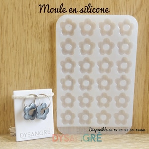 Peut inclure: Un moule en silicone transparent avec des cavités en forme de fleurs, à côté d'une paire de boucles d'oreilles fleurs grises sur une carte blanche. La carte porte le texte "DYSANGRÉ". Le moule a le texte "Disponible en 15-20-25-30-35mm".