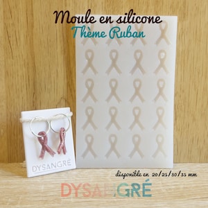 Op de afbeelding: Een witte siliconen mal met lintvormen, naast een paar roze glitter lint oorbellen op een witte kaart. De kaart leest "DYSANGRE". De mal is gelabeld "Moule en silicone Thème Ruban".