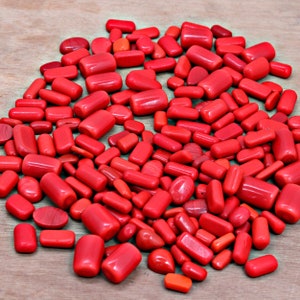 May include: A large pile of red coral stones, some are smooth and others are rough, all are a vibrant red color.