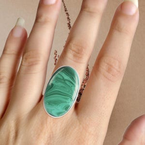 May include: A silver ring with a large oval green malachite stone. The stone has a swirling pattern.
