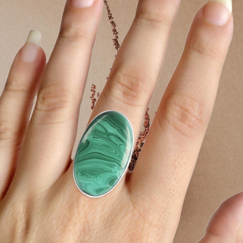 May include: A silver ring with a large oval green malachite stone. The stone has a swirling pattern.