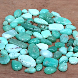May include: A collection of green and blue gemstone cabochons, also known as green opal or chrysoprase. The stones are various shapes and sizes, and have a smooth, polished finish.