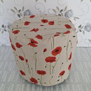 Può includere: Un pouf beige con un vivace motivo floreale di papaveri rossi. Il poggiapiedi rivestito in tessuto presenta un motivo ripetuto di papaveri rossi con steli e foglie verdi. Il pouf rotondo e imbottito aggiunge un tocco di arredamento ispirato alla natura.