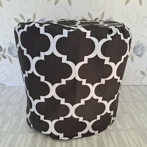 Può includere: Una copertura in tessuto a fantasia bianca e nera, probabilmente per un elettrodomestico da cucina. Il motivo è un disegno a quadrifoglio ripetuto. La copertura cilindrica sembra essere realizzata in un materiale robusto.