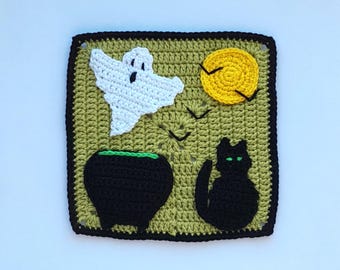 May include: A crocheted Halloween-themed square featuring a white ghost, a yellow moon, black birds, a black cauldron with green trim, and a black cat with green eyes. The square has a green background with a black border.