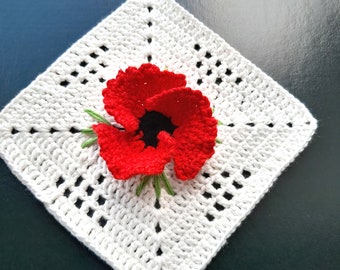 May include: White crocheted square with a red crocheted poppy flower in the center.