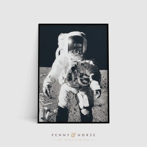May include: A black and white photograph of an astronaut standing on the moon. The astronaut is wearing a spacesuit and a helmet. The surface of the moon is visible in the background.