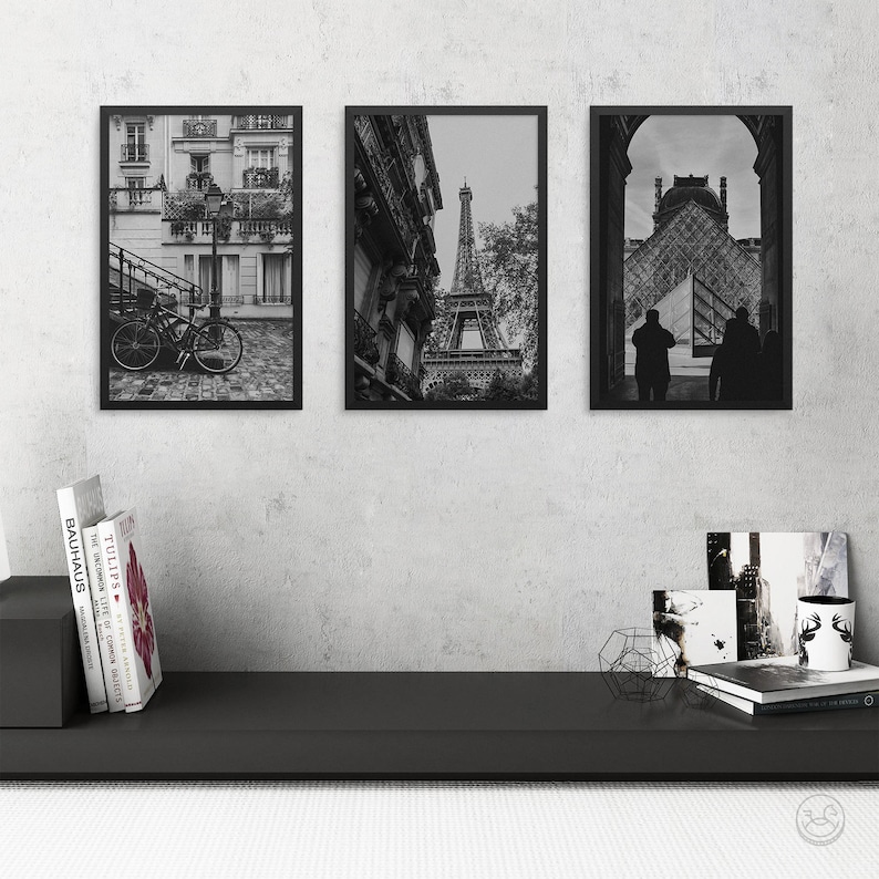 May include: Three black framed photographs of Paris, France. The left photo shows a bicycle parked on a cobblestone street. The middle photo shows the Eiffel Tower from a street level perspective. The right photo shows a silhouette of two people walking in front of a building.