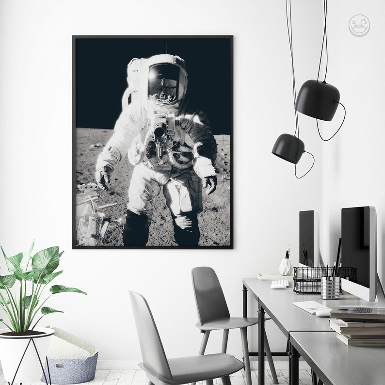 May include: Black and white photograph of an astronaut walking on the moon. The astronaut is wearing a spacesuit and helmet. The surface of the moon is visible in the background.