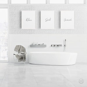 May include: White bathroom with a white bathtub, a white chair with a gray blanket, and three framed prints on the wall that say "Relax", "Soak", and "Unwind".