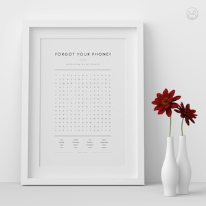 Op de afbeelding: Een ingelijst afdruk met een zwart-witte woordzoeker. De titel van de puzzel is "Forgot Your Phone?" en de ondertitel is "Bathroom Word Search". De puzzel is gevuld met letters en de woorden die je moet vinden staan onder de puzzel. De afdruk is op een witte achtergrond en is ingelijst in een wit frame.