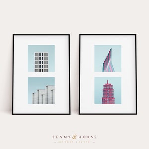May include: Two framed prints of architectural buildings. The print on the left shows a white building with a blue sky. The print on the right shows a pink and blue building with a blue sky.