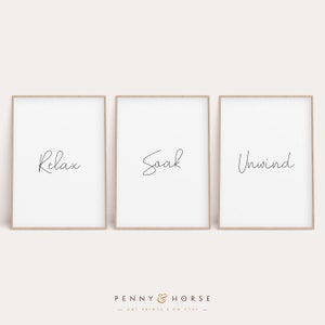 May include: Three framed prints with the words "Relax", "Soak", and "Unwind" in a simple, handwritten font. The prints are on a white background and have a light wood frame.