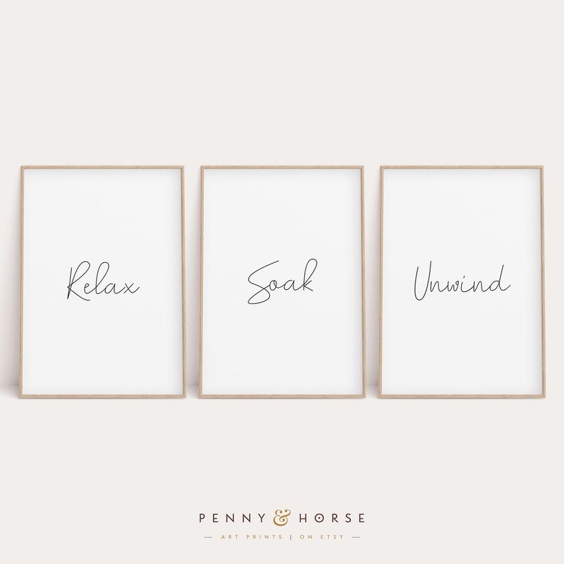 May include: Three framed prints with the words "Relax", "Soak", and "Unwind" in a simple, handwritten font. The prints are on a white background and have a light wood frame.