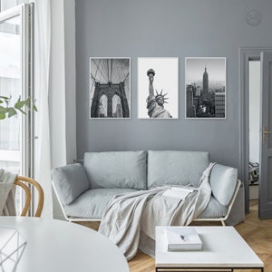 May include: Three black and white framed photographs of New York City landmarks. The photos show the Brooklyn Bridge, the Statue of Liberty, and the Empire State Building.