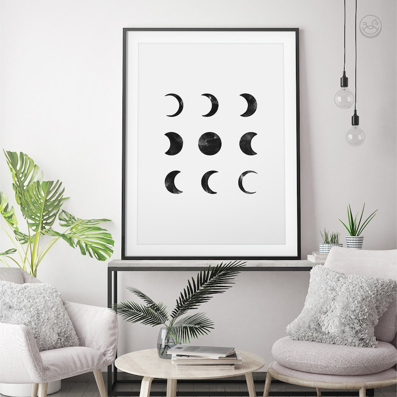 May include: Black and white minimalist art print featuring a grid of nine moons in various phases. The print is framed in a black frame and hanging on a white wall.