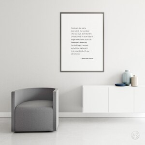 May include: A framed print with a quote by Ralph Waldo Emerson hangs above a white cabinet. The quote reads, "Finish each day and be done with it...Tomorrow is a new day." A gray armchair sits to the left. Decorative vases and a plate are on the cabinet.