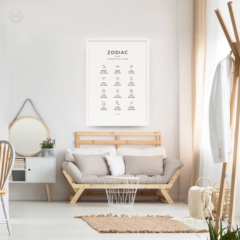 May include: A white framed poster with the word "Zodiac" and astrological signs in black and white. The poster is hanging on a white wall in a living room setting with a couch, a side table, and a plant.