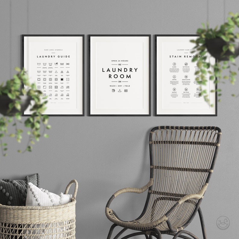May include: Three framed laundry room prints with black frames and white backgrounds. The prints include laundry symbols, laundry room text, and stain removal tips. A wicker chair and basket with pillows are in the foreground.