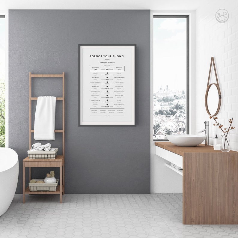 Op de afbeelding: Een ingelijst print met de tekst "Forgot your phone?" en een lijst met veelvoorkomende uitspraken en hun bijbehorende emoji. De print hangt aan een grijze muur in een badkamer met een witte tegelvloer, een houten wastafel en een wit bad.