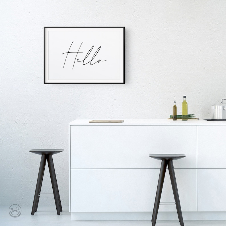 K&ouml;nnte beinhalten: Eine wei&szlig;e K&uuml;chenarbeitsplatte mit zwei schwarzen Hockern und einem gerahmten Druck mit der Aufschrift "Hello" an der Wand.