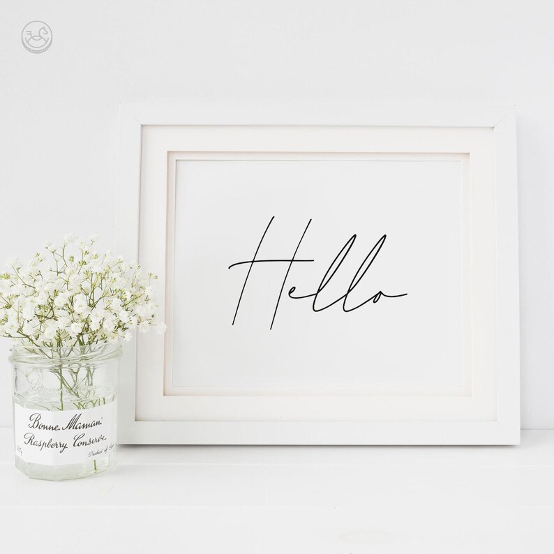 K&ouml;nnte beinhalten: Ein wei&szlig;er gerahmter Druck mit dem Wort "Hello" in schwarzer Kursivschrift. Der Druck liegt auf einer wei&szlig;en Oberfl&auml;che mit einem kleinen Glas mit wei&szlig;en Blumen davor.