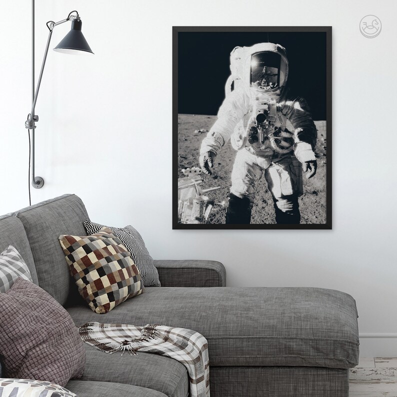 May include: A black and white photograph of an astronaut in a spacesuit standing on the moon. The astronaut is wearing a helmet and is holding a camera. The background is a dark, starry sky.